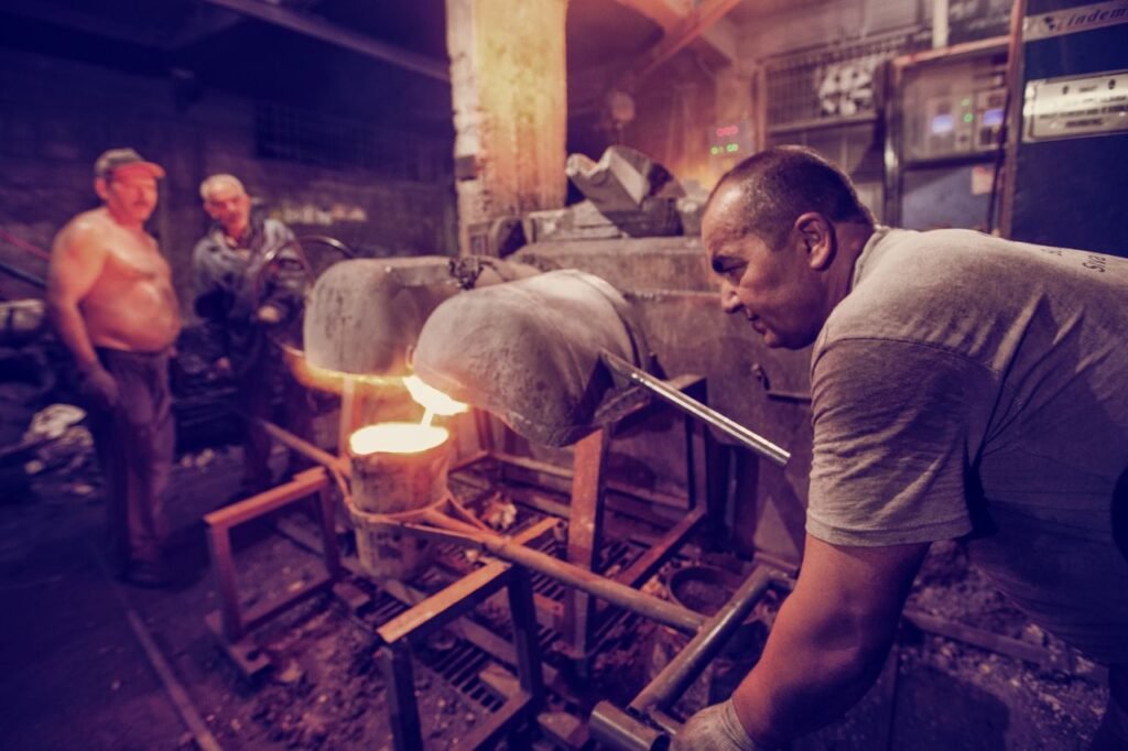 Skilled metalworkers manage a high-temperature industrial furnace in a factory setting.