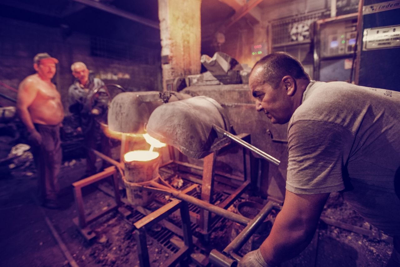 Skilled metalworkers manage a high-temperature industrial furnace in a factory setting.