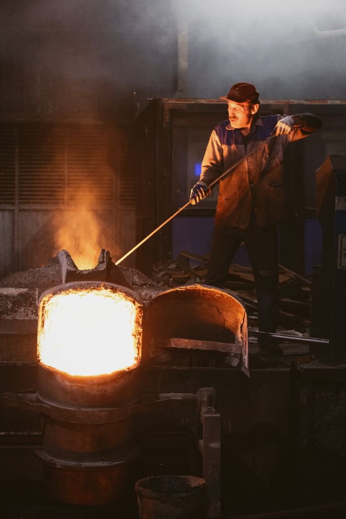 A skilled worker managing molten metal in an industrial setting, ensuring safety and precision.